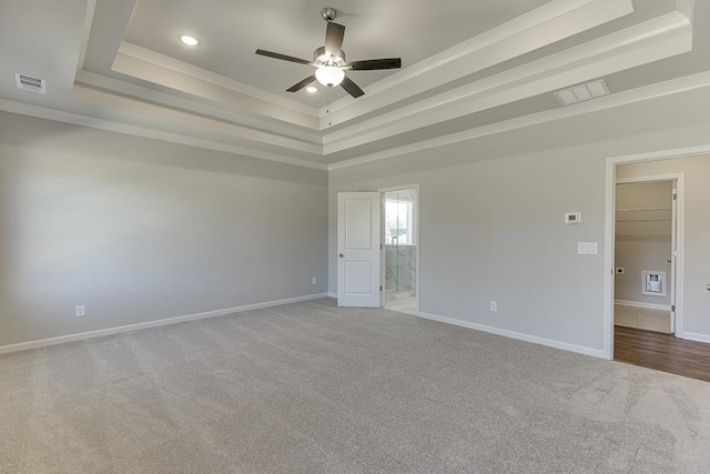 carpeted empty room featuring visible vents, a raised ceiling, baseboards, and ornamental molding