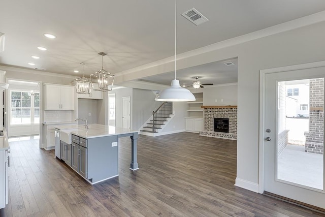 kitchen featuring visible vents, a brick fireplace, crown molding, light countertops, and white cabinetry