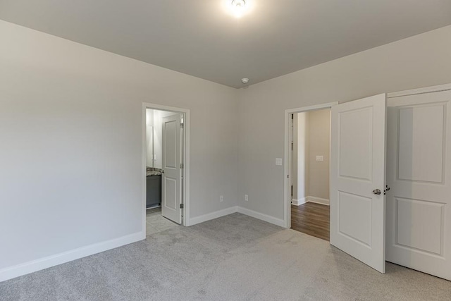 unfurnished bedroom featuring light carpet, ensuite bathroom, and baseboards