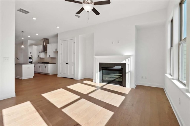 unfurnished living room with ceiling fan, sink, and light hardwood / wood-style floors