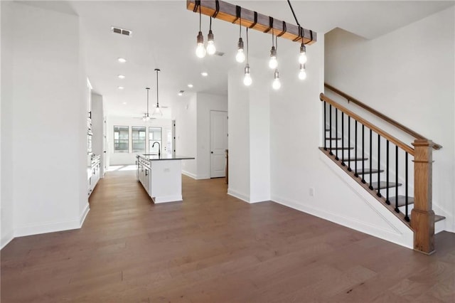 kitchen with dark hardwood / wood-style floors, sink, white cabinets, hanging light fixtures, and a kitchen island with sink