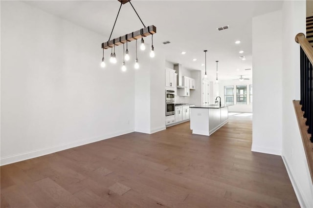 unfurnished living room featuring dark hardwood / wood-style floors, white cabinetry, sink, hanging light fixtures, and a center island with sink