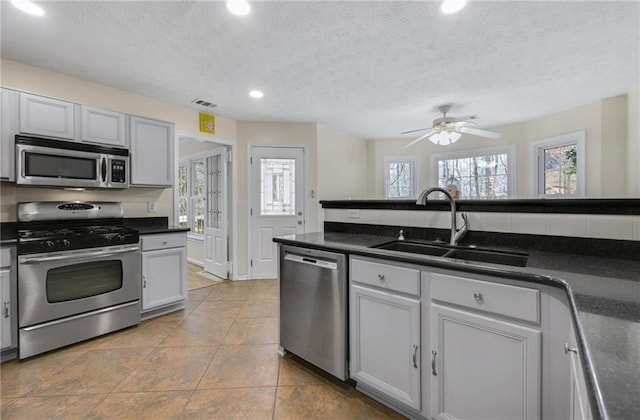 kitchen featuring stainless steel appliances, dark countertops, a sink, and visible vents