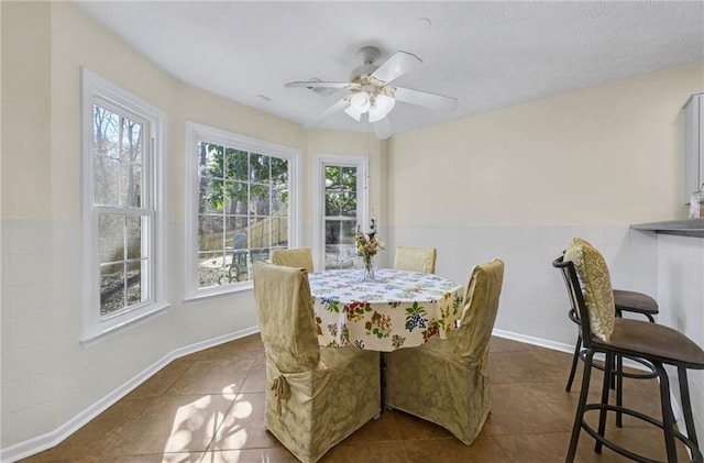 dining space with ceiling fan, a textured ceiling, a wainscoted wall, dark tile patterned flooring, and tile walls