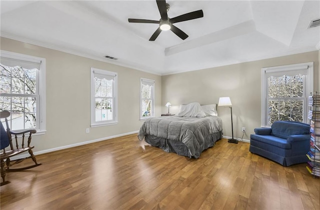 bedroom with wood finished floors, a raised ceiling, visible vents, and baseboards