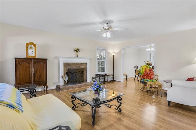 living room featuring light wood finished floors, a fireplace, a ceiling fan, and baseboards