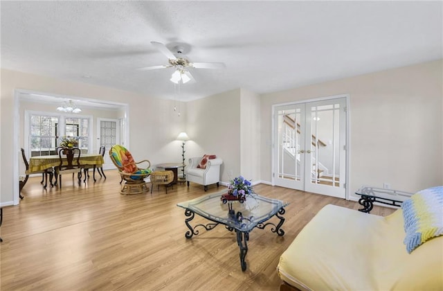 living room featuring a textured ceiling, ceiling fan with notable chandelier, wood finished floors, baseboards, and french doors