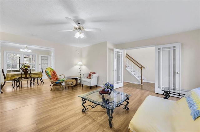 living area with a textured ceiling, stairs, wood finished floors, and ceiling fan with notable chandelier