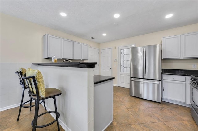 kitchen featuring dark countertops, appliances with stainless steel finishes, a kitchen breakfast bar, a textured ceiling, and recessed lighting