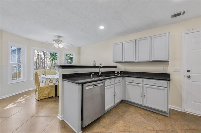 kitchen with dark countertops, visible vents, stainless steel dishwasher, a sink, and a peninsula