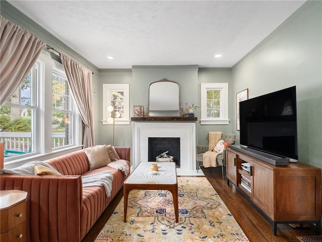 living area featuring a fireplace with flush hearth, crown molding, dark wood-type flooring, and recessed lighting