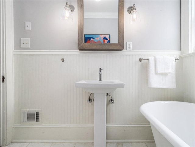 bathroom with a freestanding bath, wainscoting, and visible vents