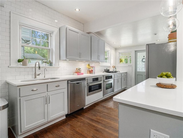 kitchen featuring dark wood-style floors, decorative light fixtures, stainless steel appliances, light countertops, and a sink