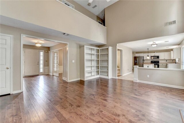 12060 Carriage Park Ln, Duluth, GA 30097 - unfurnished living room featuring wood finished floors, a towering ceiling, ceiling fan, baseboards, and a sink