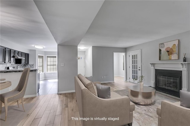 living area featuring light wood-type flooring, baseboards, and a glass covered fireplace