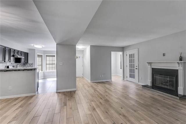 unfurnished living room featuring a glass covered fireplace, light wood-style flooring, and baseboards