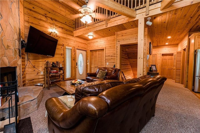 living room with ceiling fan, wooden walls, a high ceiling, carpet, and a fireplace