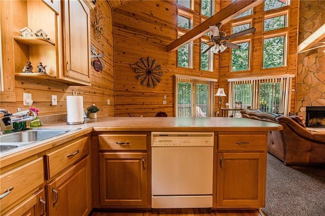 kitchen featuring a stone fireplace, wooden walls, white dishwasher, and kitchen peninsula