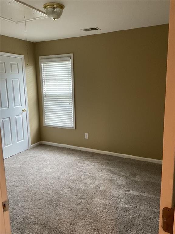 carpeted spare room with baseboards, visible vents, and attic access