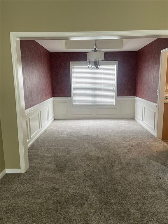 unfurnished dining area featuring wainscoting, carpet flooring, and an inviting chandelier