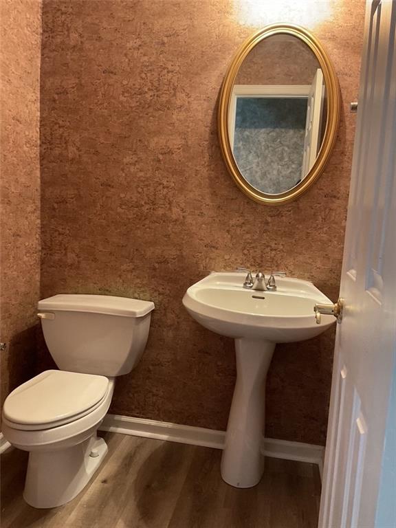 half bathroom featuring toilet, baseboards, and wood finished floors