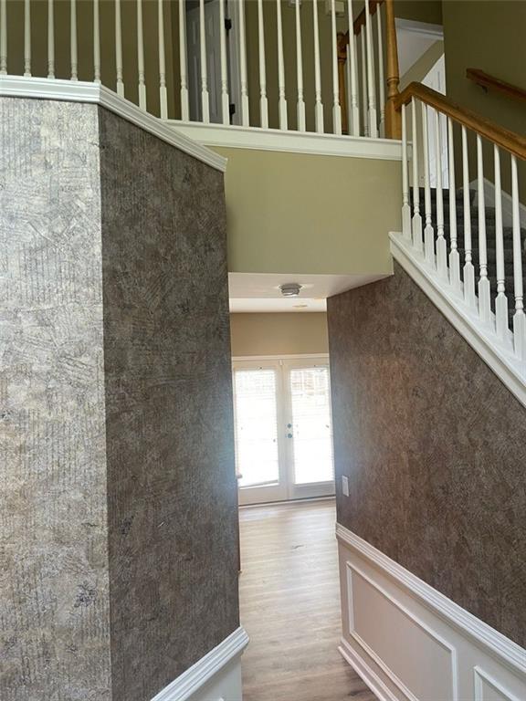 stairway with french doors, a decorative wall, a towering ceiling, wainscoting, and wood finished floors