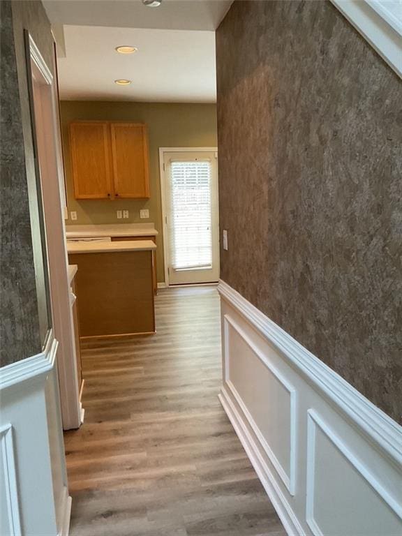 hall featuring light wood-type flooring, a wainscoted wall, and recessed lighting