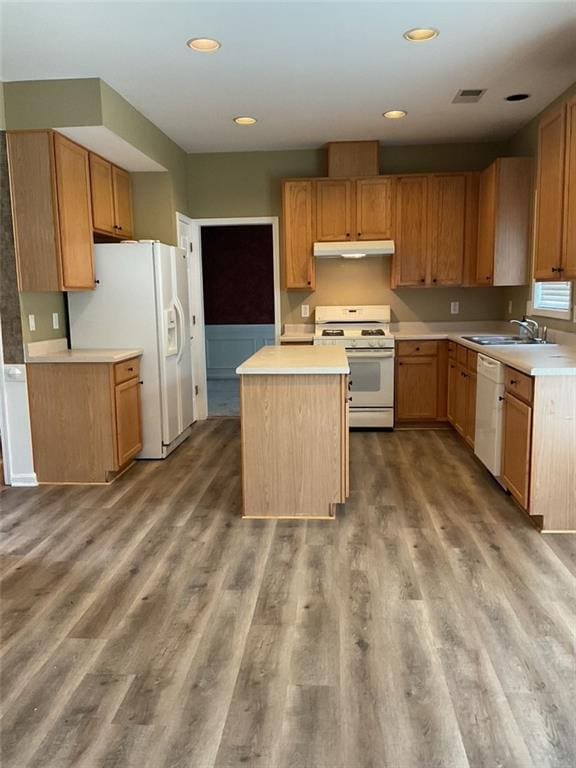 kitchen featuring white appliances, wood finished floors, light countertops, under cabinet range hood, and a sink