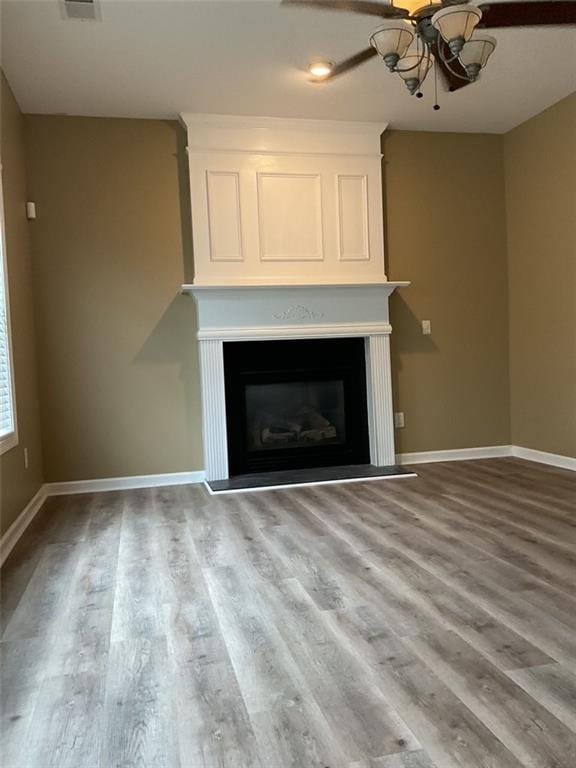 unfurnished living room with ceiling fan, a fireplace, baseboards, and wood finished floors