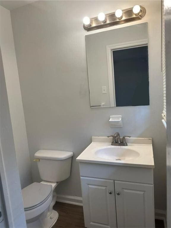 half bathroom with vanity, baseboards, wood finished floors, and toilet