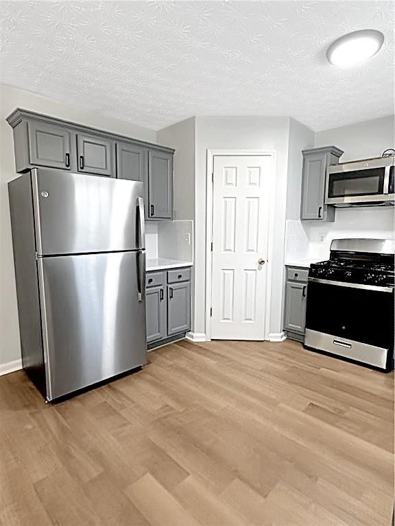 kitchen with dark hardwood / wood-style flooring, gray cabinets, a textured ceiling, and appliances with stainless steel finishes