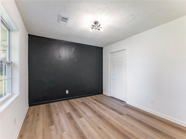 empty room featuring baseboards, visible vents, a textured ceiling, and light wood-style floors