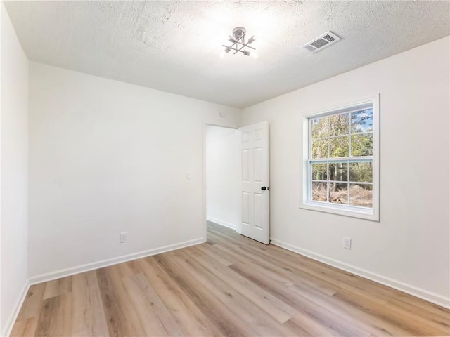 spare room with baseboards, a textured ceiling, visible vents, and light wood-style flooring