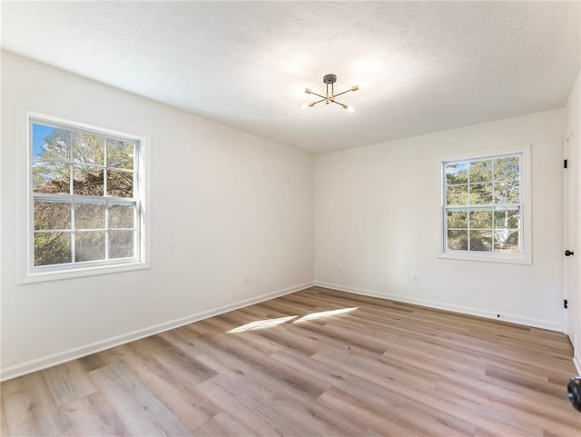 empty room featuring baseboards, an inviting chandelier, a healthy amount of sunlight, and light wood-style flooring