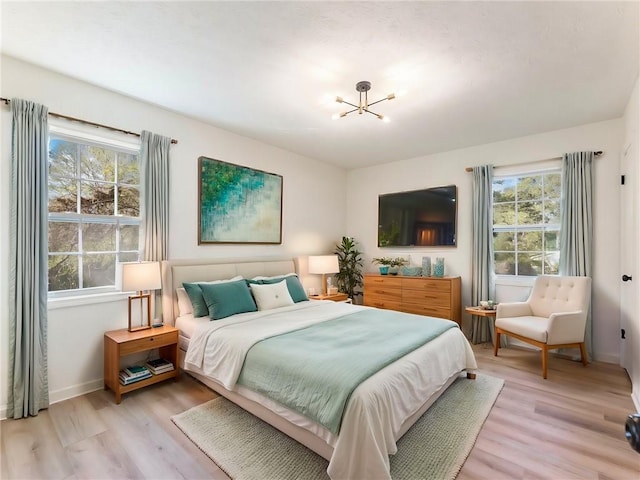 bedroom with light wood finished floors, baseboards, and an inviting chandelier
