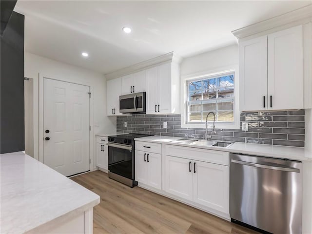 kitchen with white cabinets, backsplash, a sink, light wood-style flooring, and appliances with stainless steel finishes