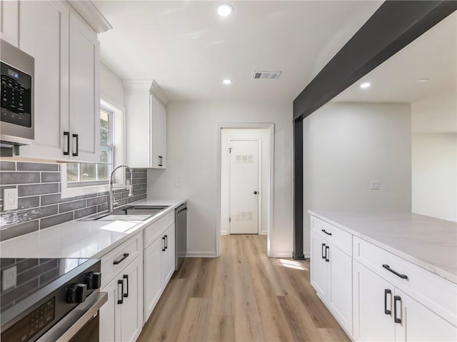 kitchen featuring tasteful backsplash, a sink, light wood-style floors, stainless steel appliances, and visible vents