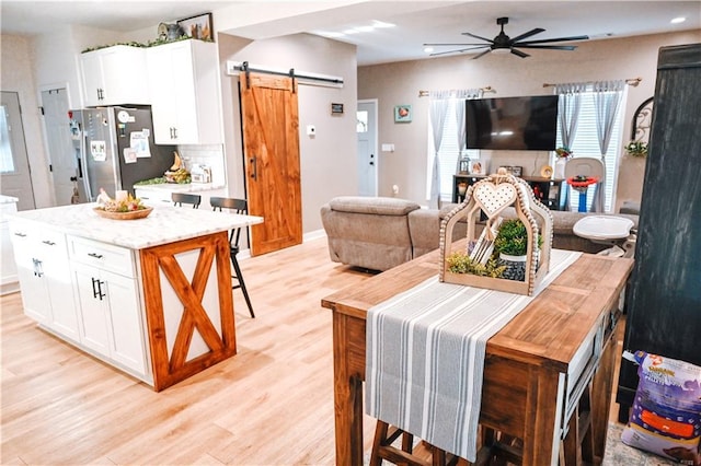 kitchen featuring a barn door, white cabinets, a ceiling fan, freestanding refrigerator, and light wood-type flooring