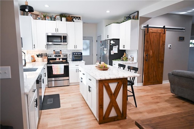 kitchen with a barn door, stainless steel appliances, a breakfast bar, light stone countertops, and tasteful backsplash