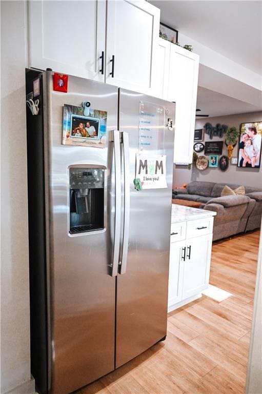 kitchen with white cabinets, open floor plan, light wood finished floors, and stainless steel fridge