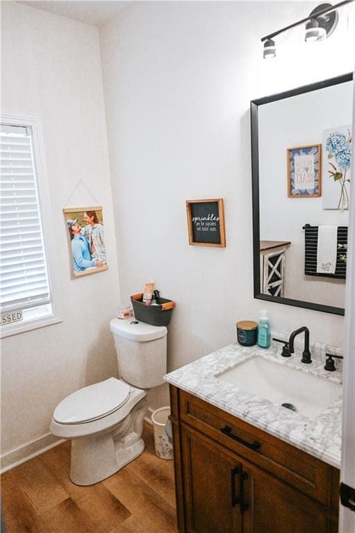 half bath with wood finished floors, toilet, and vanity
