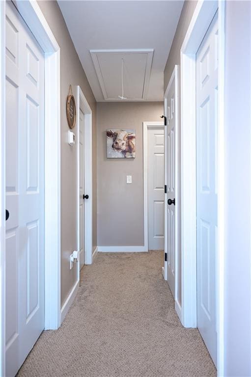 hallway with attic access, baseboards, and light carpet