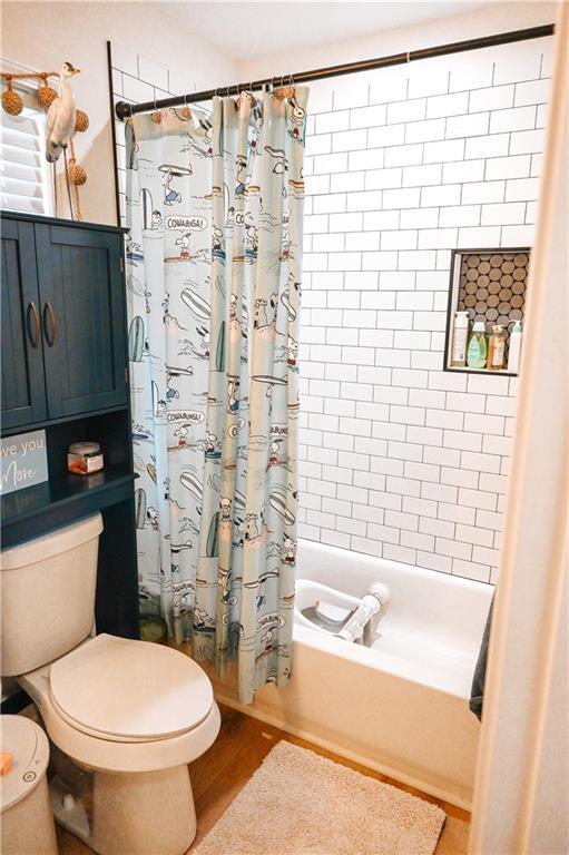 bathroom with toilet, wood finished floors, and shower / bathtub combination with curtain