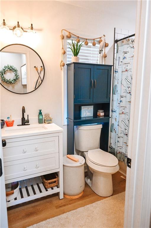 full bathroom with a shower with shower curtain, wood finished floors, toilet, and vanity