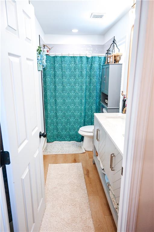 bathroom featuring wood finished floors, vanity, curtained shower, toilet, and visible vents