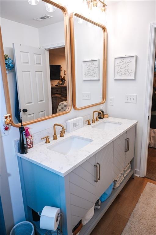 bathroom featuring wood finished floors, a sink, visible vents, and double vanity