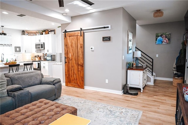 living area with light wood-type flooring, visible vents, ceiling fan, and a barn door