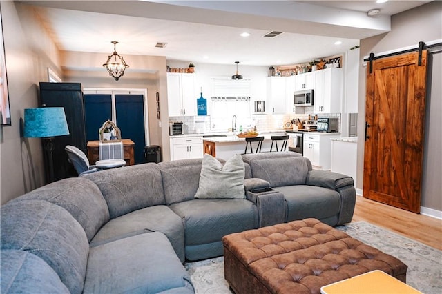 living area with a barn door, light wood-style floors, visible vents, and recessed lighting
