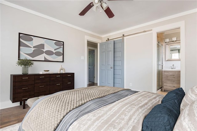 bedroom featuring a sink, wood finished floors, a barn door, crown molding, and ceiling fan