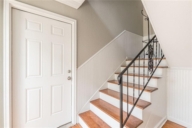 staircase featuring wainscoting, a textured wall, and wood finished floors